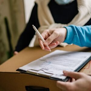 Close-up of a person signing a delivery document placed on a large cardboard box indoors.